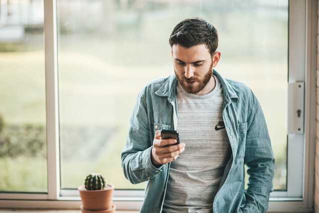 guy with beard and jacket holding iphone 7 scrolling through social media