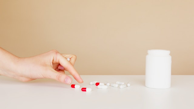 female hand picking up a red and white medication for her prescription for a chronic illness