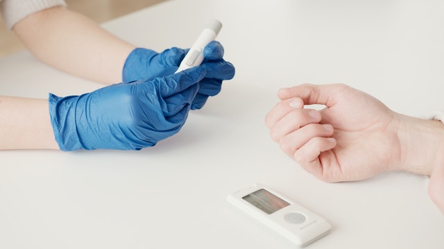 Medical doctor wearing blue latex gloves checking blood sugar levels in the clinic