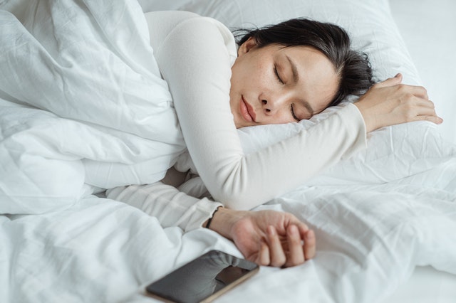 woman sleeping in bed with white duvet next to her iphone 10