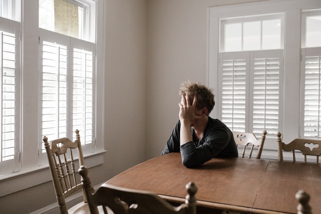 middle aged man sitting alone in the dining room feeling depressed and sad
