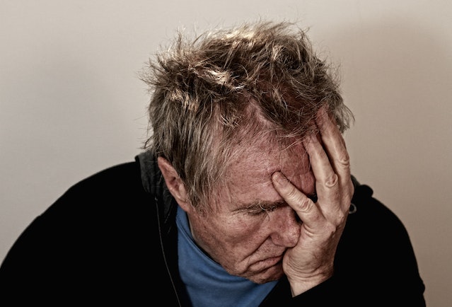 Elderly man holding his head in despair due to chronic illness struggles